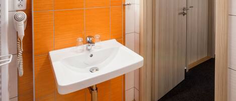 A bathroom with an orange tiled wall, a white sink, and a mirror above it.