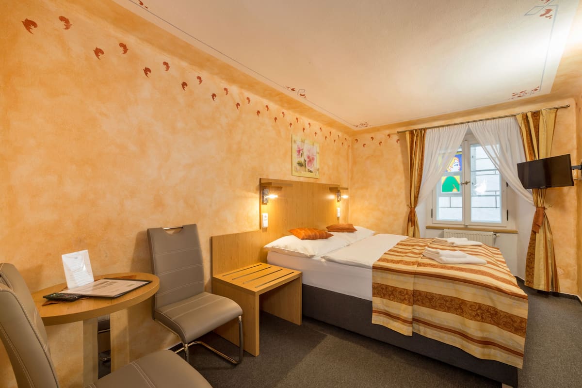 Habitación de hotel con cama, escritorio, silla, televisor y ventana con cortinas.