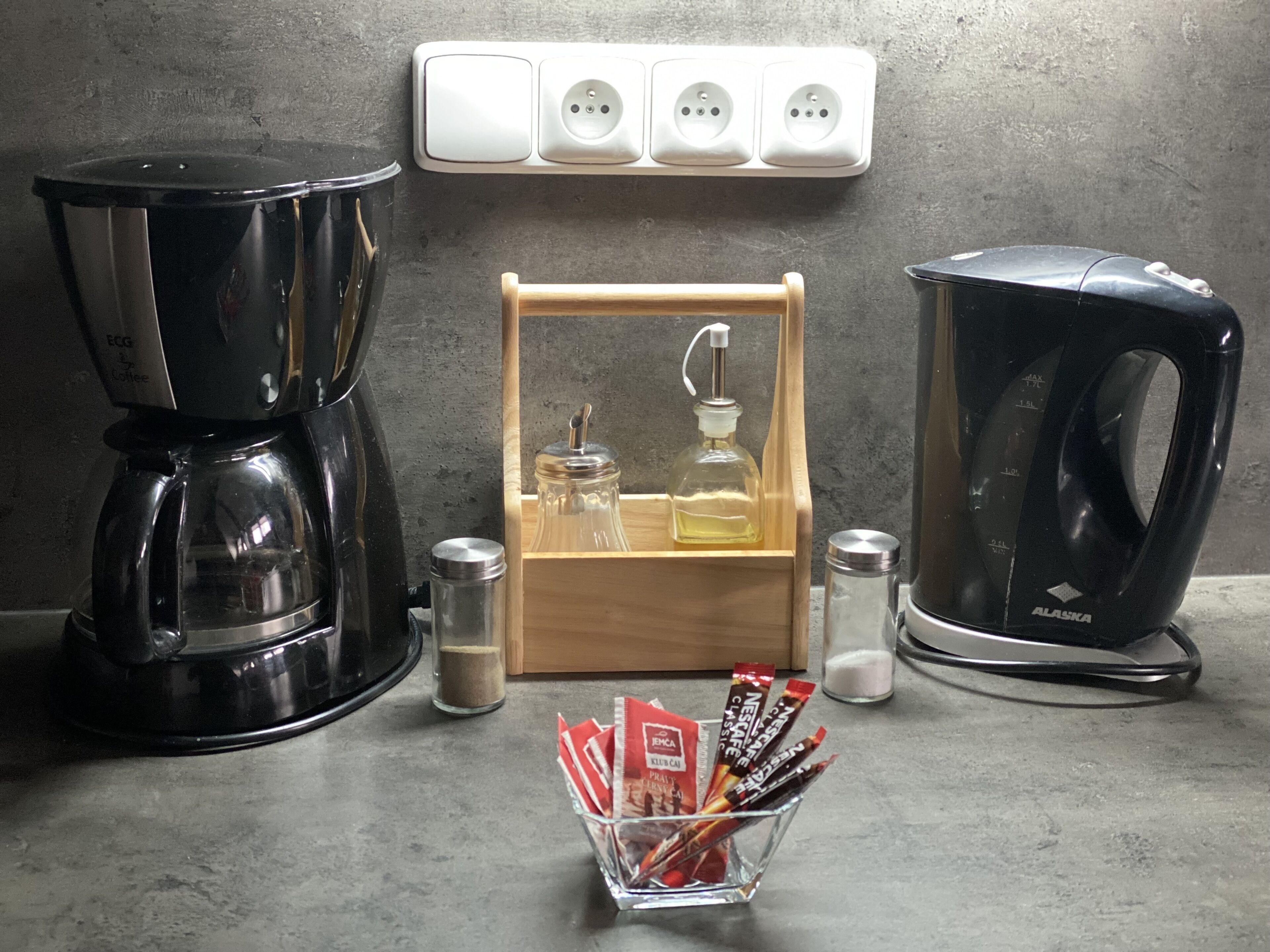 A kitchen counter with a coffee maker, a kettle, a spice rack, and a small glass jar.