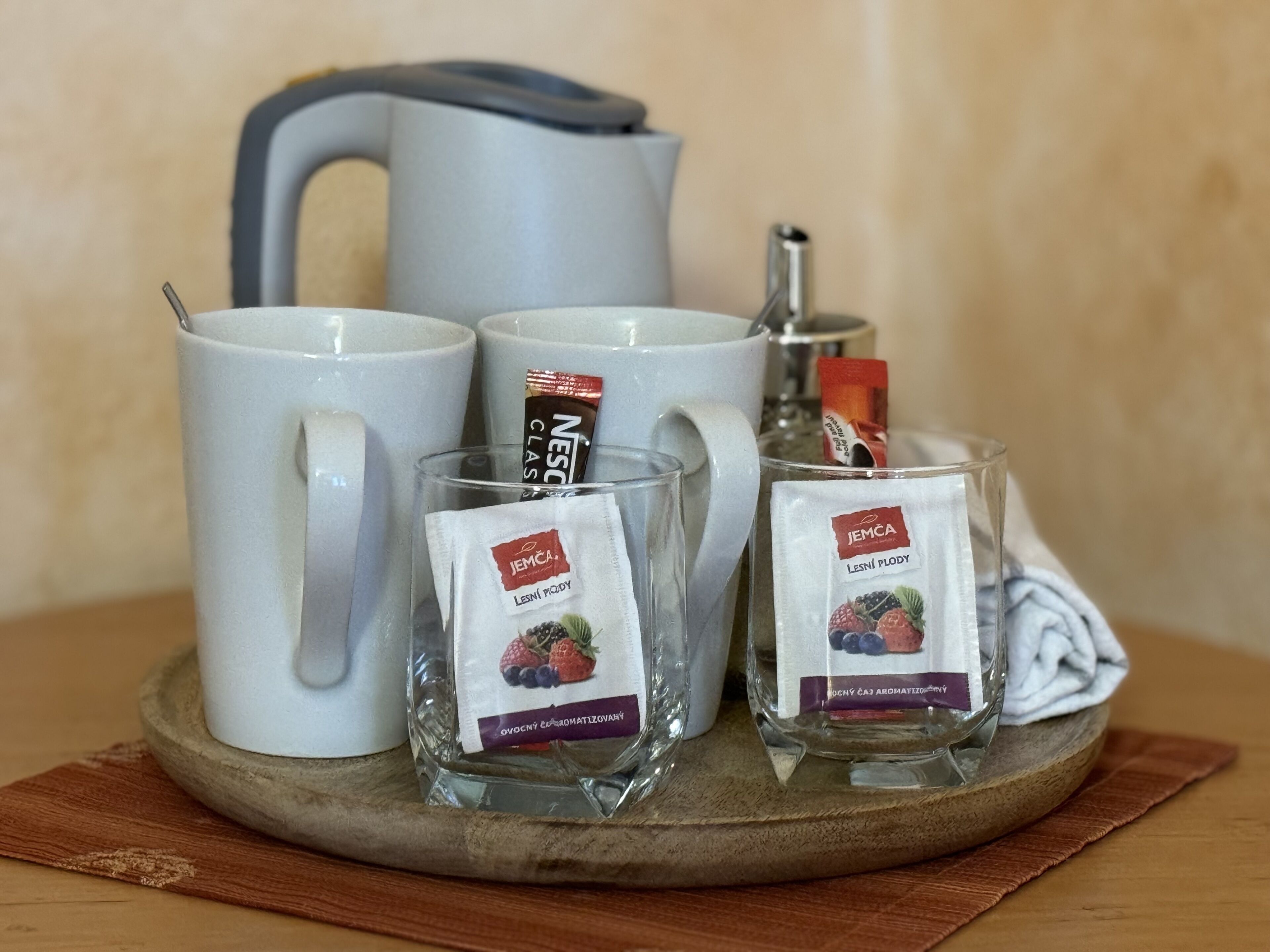 A set of white ceramic mugs, a glass teapot, and two glass cups with tea bags on a wooden tray.