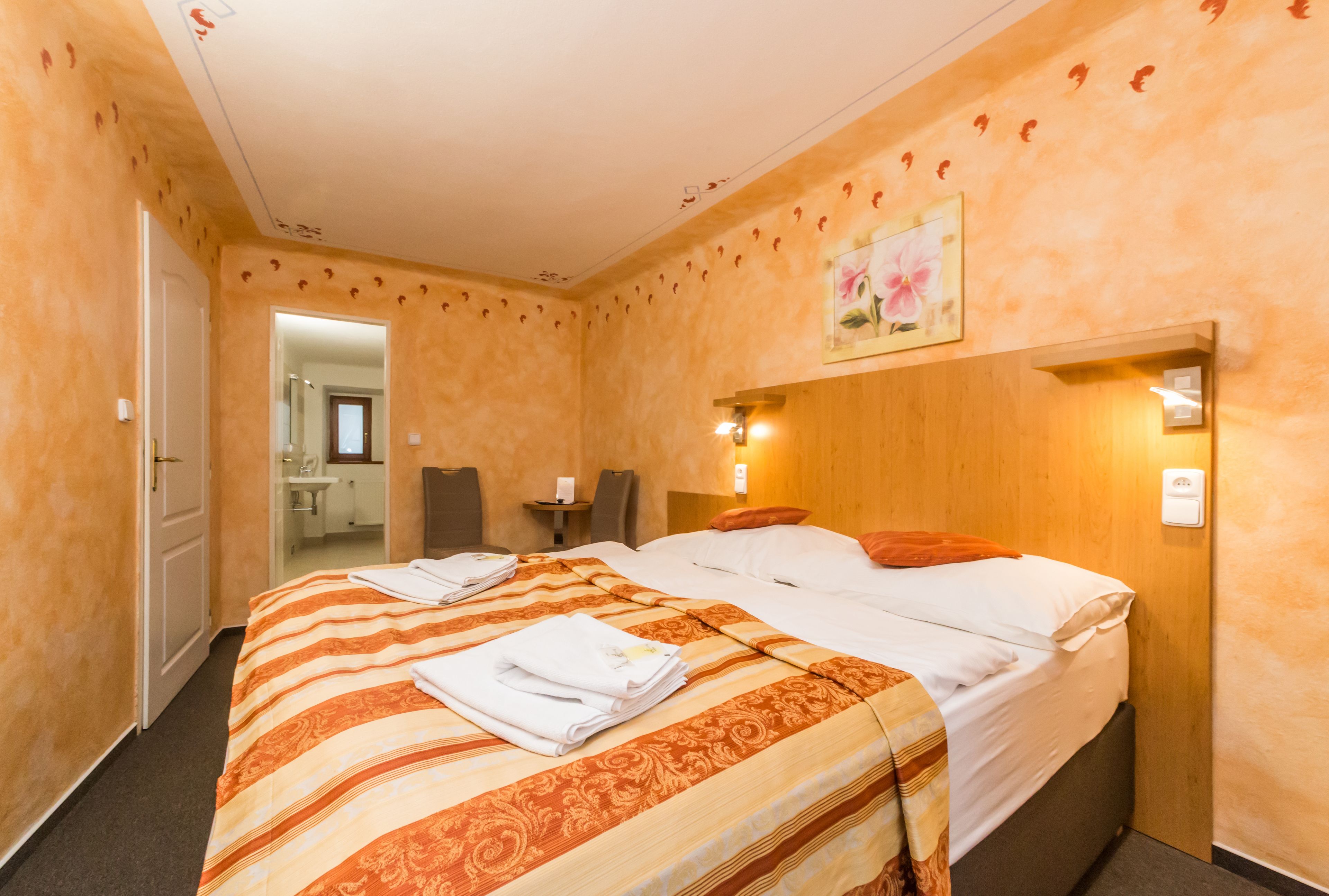 Una habitación de hotel con una cama grande, una mesita de noche, una silla y un baño visible a través de una puerta abierta.