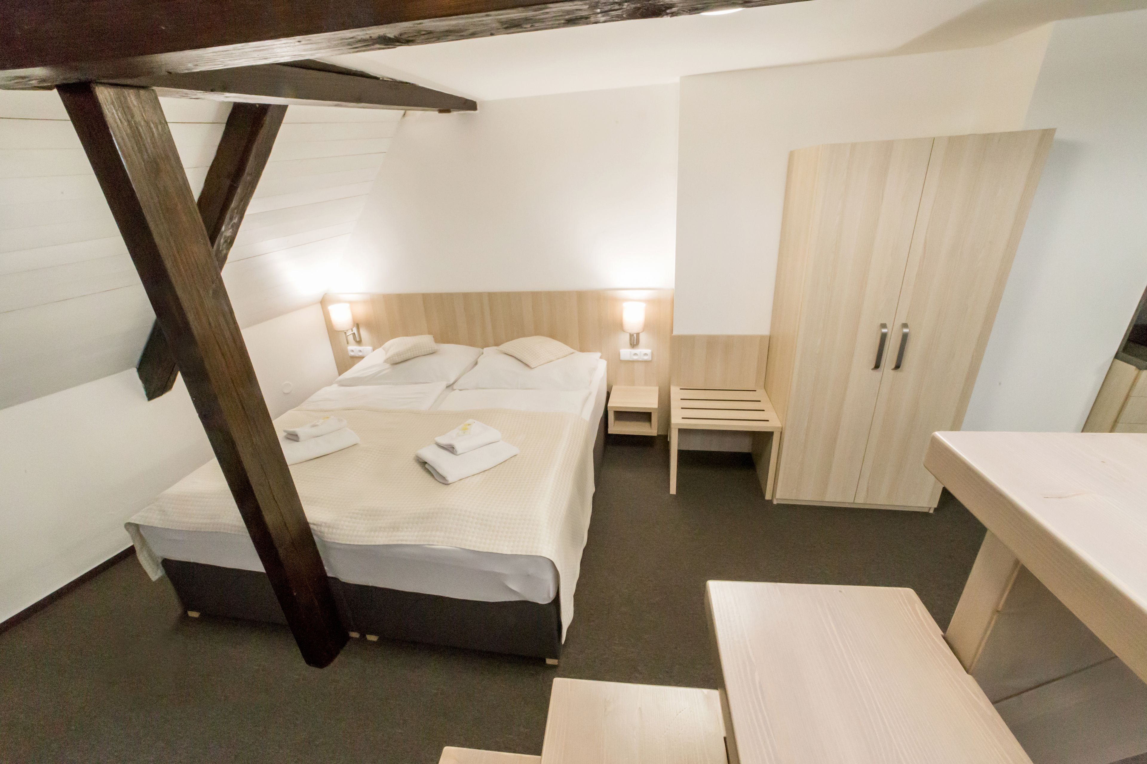 A bedroom with a bed, bedside tables, a wooden wardrobe, and a desk.