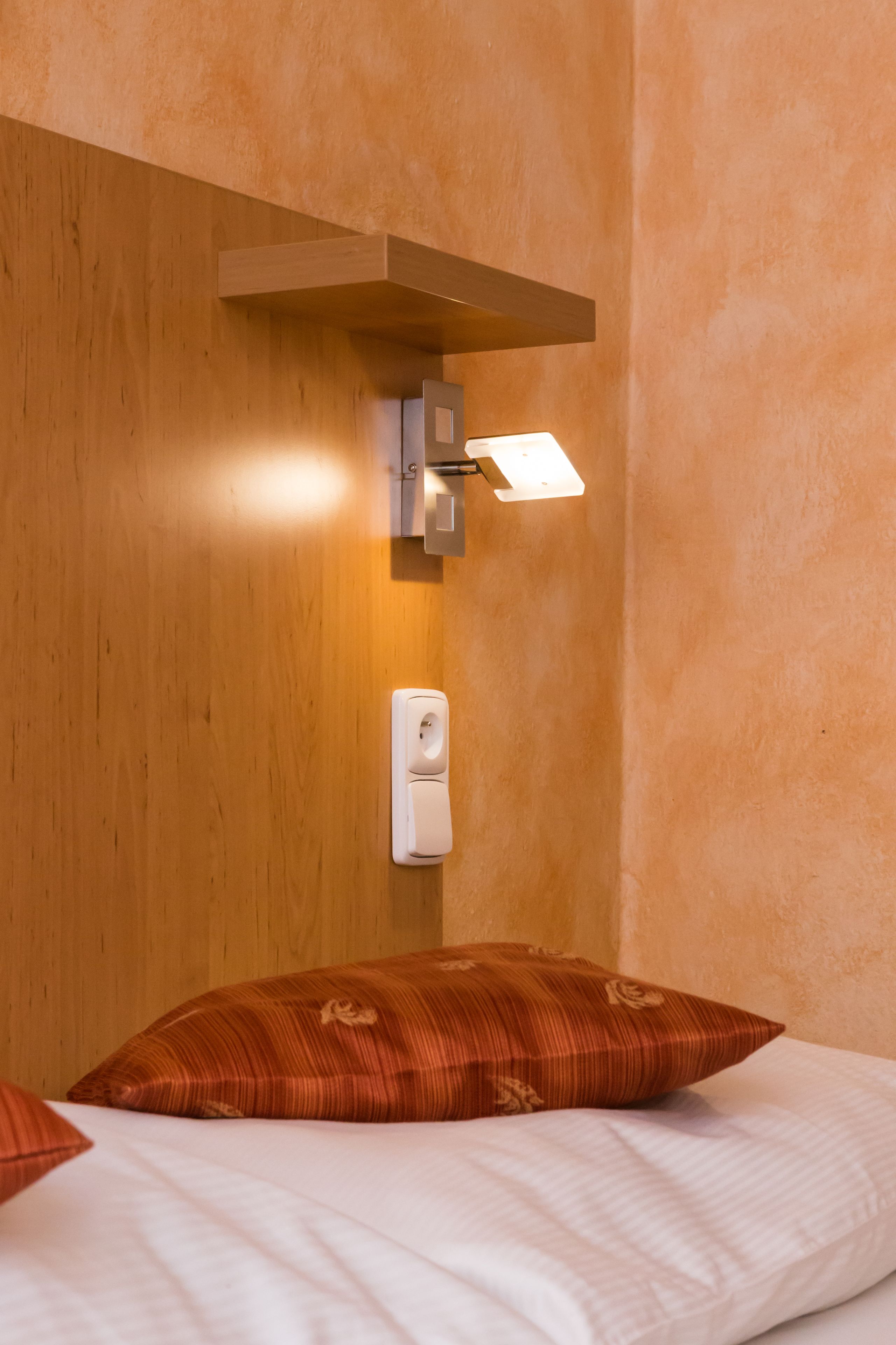 Habitación de hotel con cabecera de madera, lámpara de pared, teléfono y cama con dos almohadas.