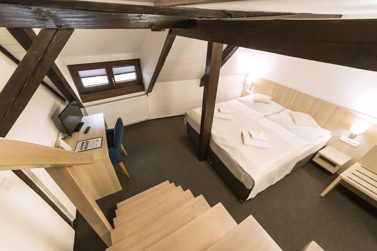 Un dormitorio con cama, escritorio, silla, ventana y escalera.