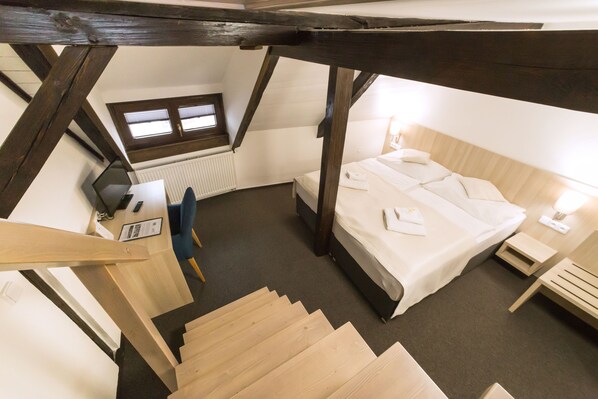 A bedroom with a bed, a desk, a chair, a window, and a staircase. - Pension Galko (Cesky Krumlov)