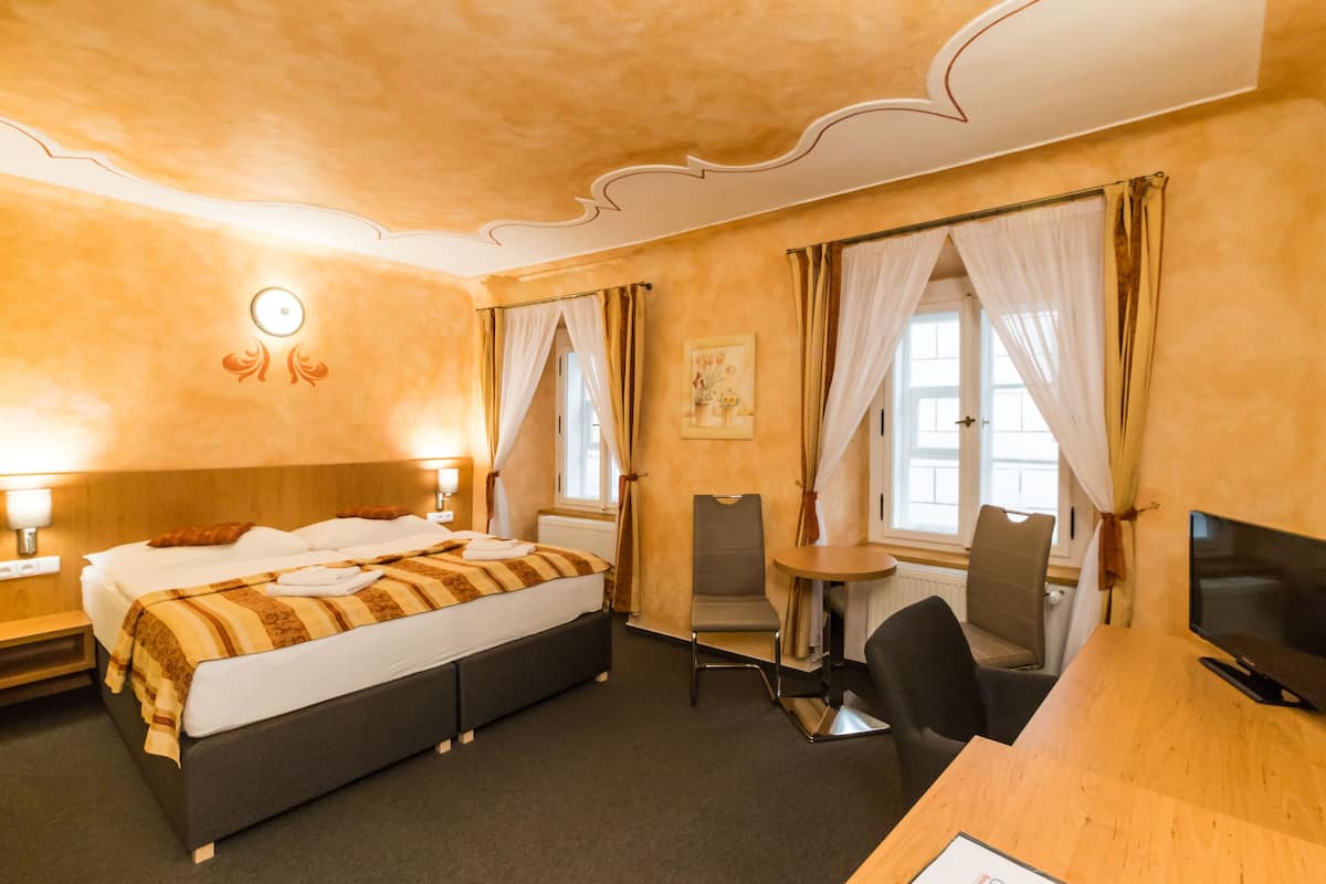 Una habitación de hotel con cama, escritorio, silla, televisor y cortinas.