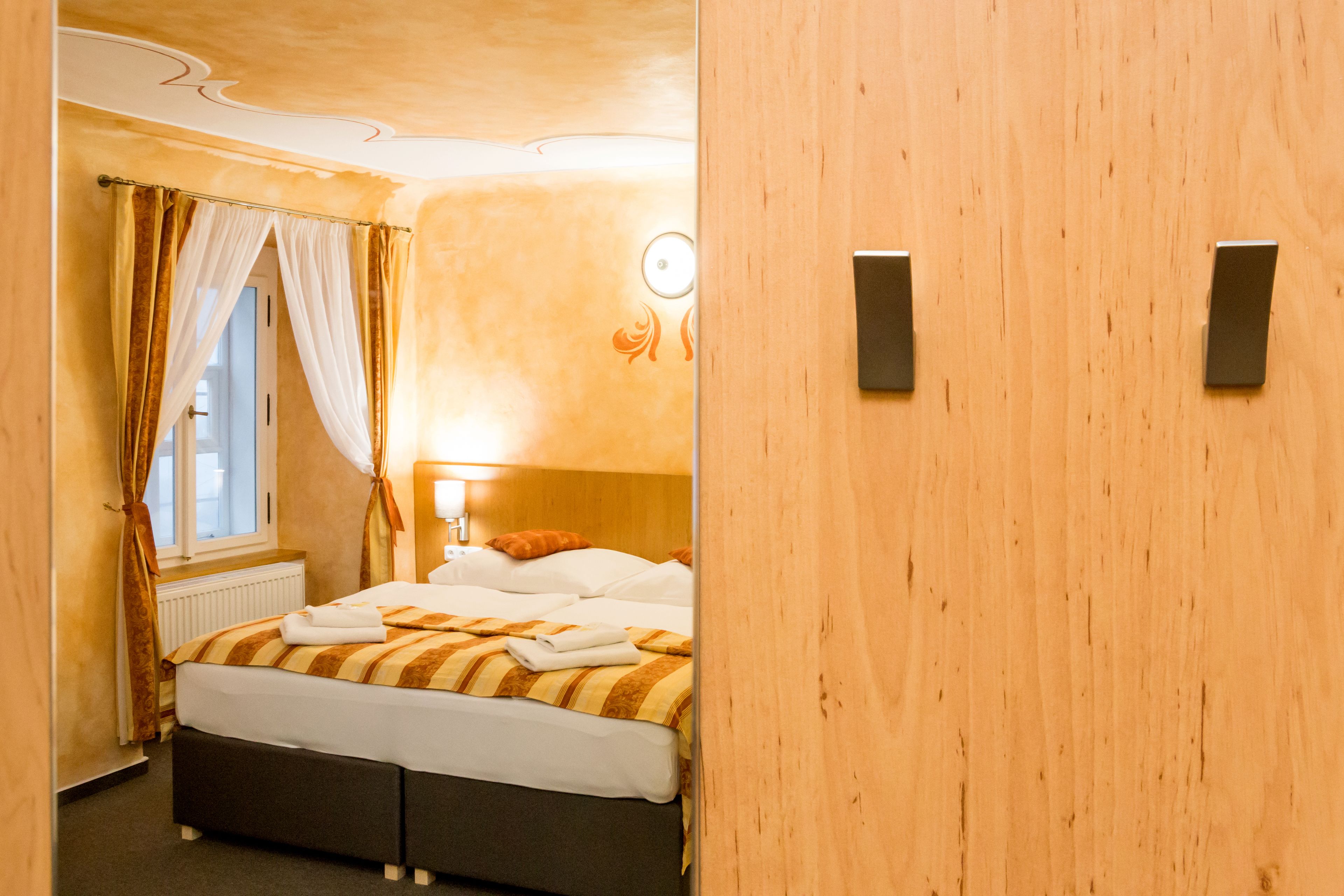 A hotel room with a bed, curtains, a radiator, and a wall-mounted light fixture.