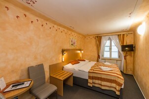 A hotel room with a bed, a desk, a chair, a TV, and a window with curtains.