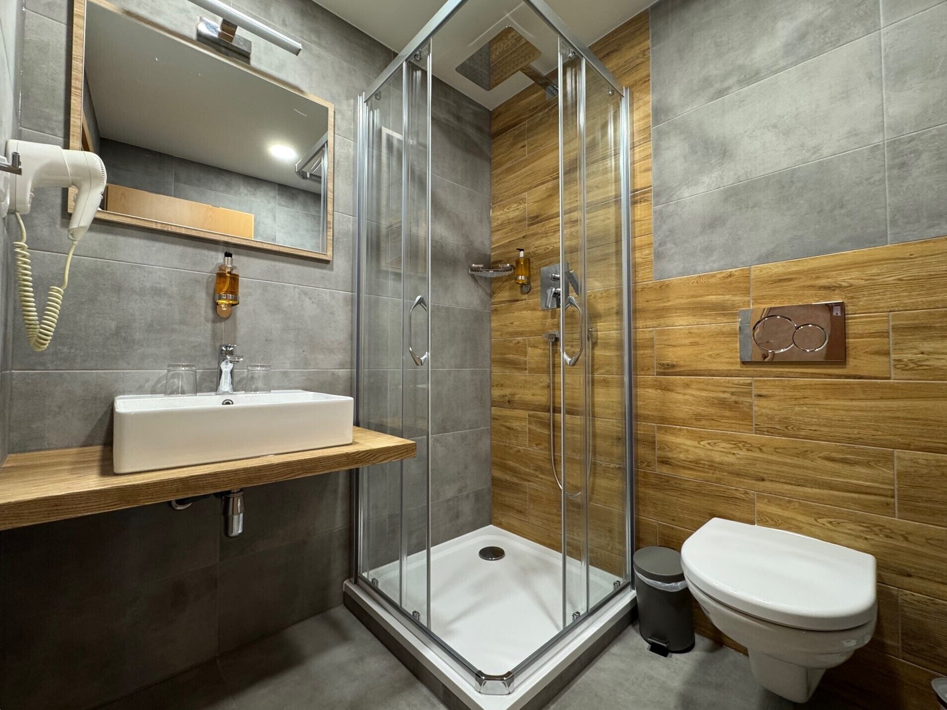 Een moderne badkamer met een douchecabine van glas, een houten wastafelmeubel en een toilet.