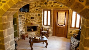 A stone-walled room with a fireplace, a wooden table, and a sofa. - Diktynna Luxury Villas (Ierapetra)