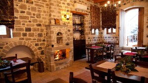 A stone-walled room with a fireplace, wooden tables, and chairs. - Diktynna Luxury Villas (Ierapetra)