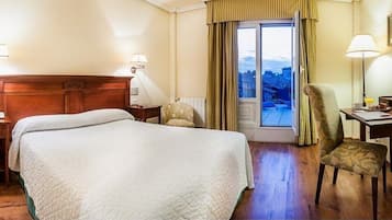 A hotel room with a large bed, a desk, a chair, and a view of the city through a window.