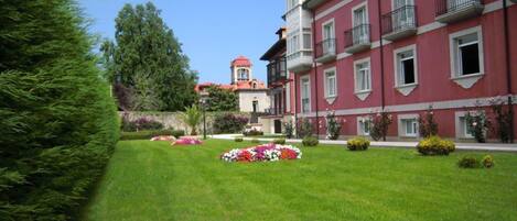 A building with a red facade and multiple windows, surrounded by well-maintained lawns and flower beds.