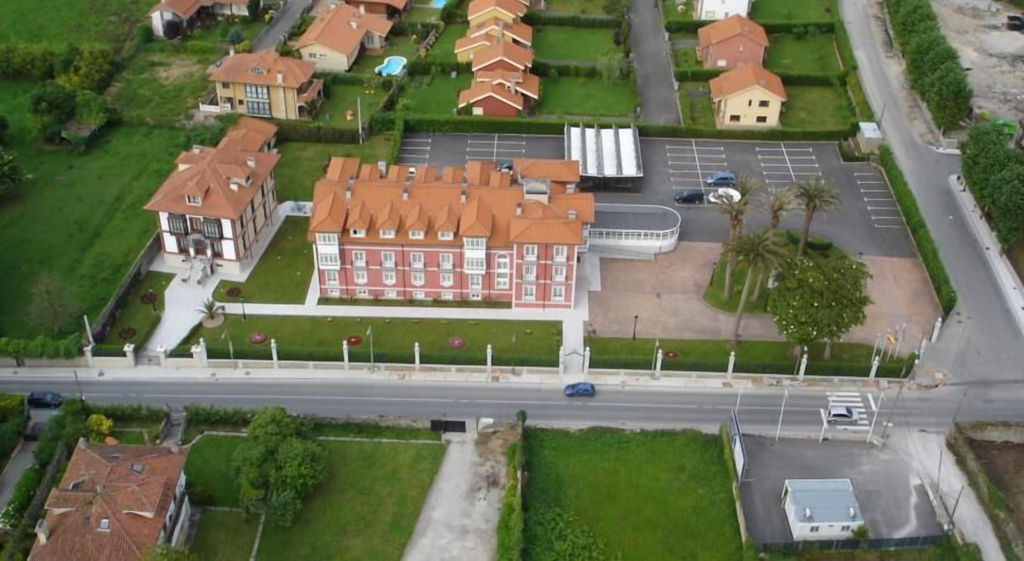 An aerial view of a residential area with a large red building, likely a hotel, surrounded by smaller houses and a parking lot.