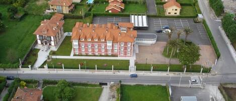 Luchtbeeld van een woongebied met een groot, rood gebouw, waarschijnlijk een hotel, omringd door kleinere huizen en een parkeerplaats.