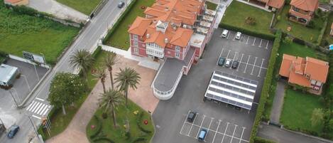Vue aérienne d’un bâtiment avec un parking, une allée sinueuse et un espace paysager agrémenté de palmiers.