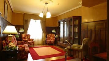 Un salón tradicional con sillones floreados, alfombra roja y un aparador de madera.