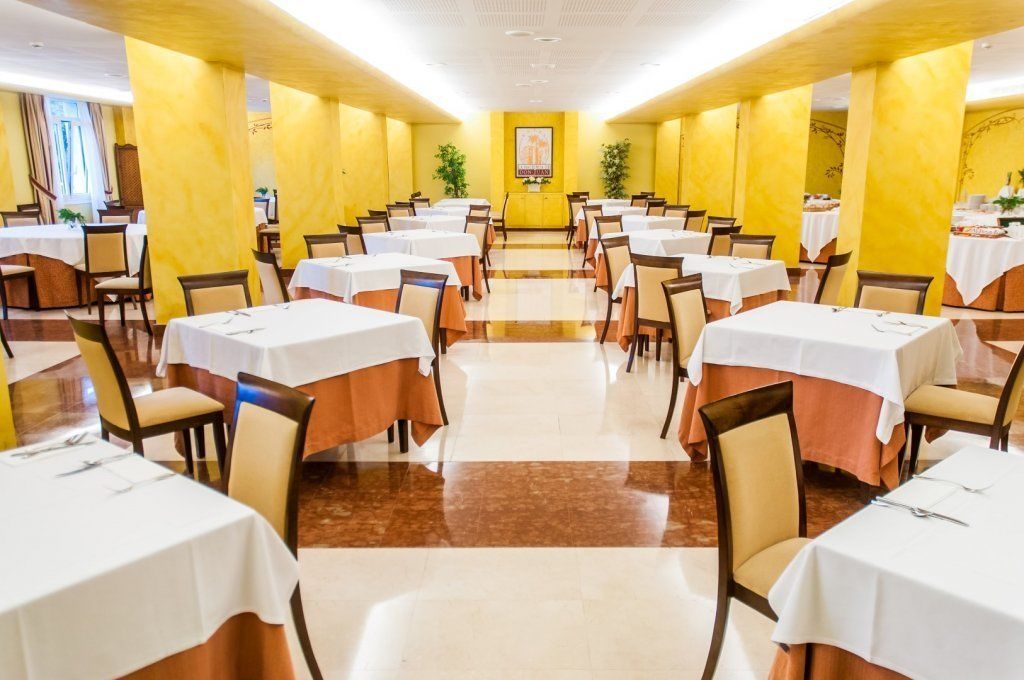A large dining hall with multiple tables and chairs, arranged in rows.