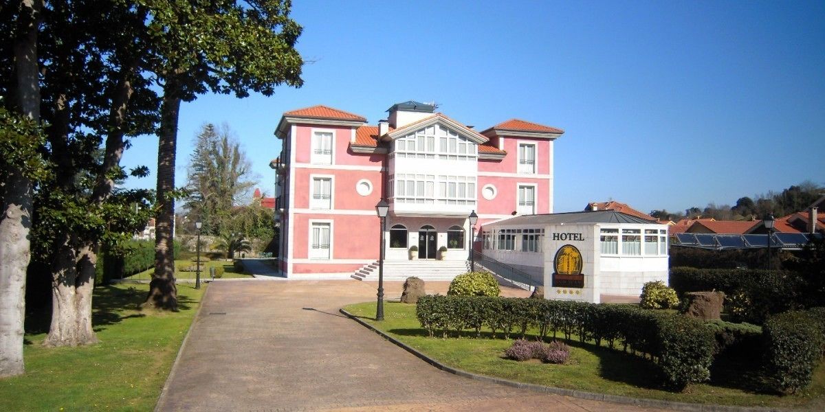 Un hotel su due piani con un ingresso centrale, un piccolo edificio aggiunto e un giardino curato.
