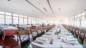 A long dining table set with white tablecloths, green chairs, and neatly arranged plates and cutlery.