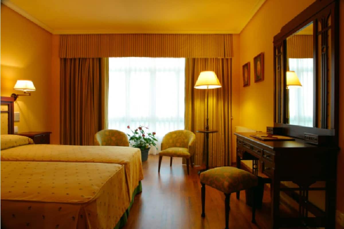 A hotel room with two beds, a desk, a television, and a large window with curtains.
