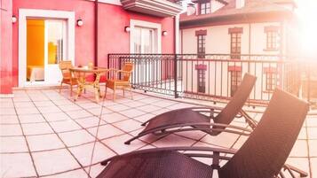 A balcony with wicker chairs and a table, a red building, and a white building with a balcony.