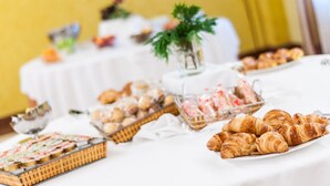 Une table de buffet garnie de diverses pâtisseries et desserts, notamment des croissants et un gâteau, le tout disposé sur une nappe blanche.