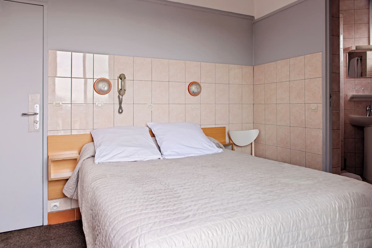 A neatly made bed with a white duvet, a wooden headboard, and two bedside lamps.