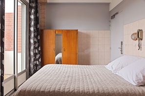 A bedroom with a bed, a wooden wardrobe, a telephone, and a view through a window with curtains. - Hôtel de la Comète (Paris)