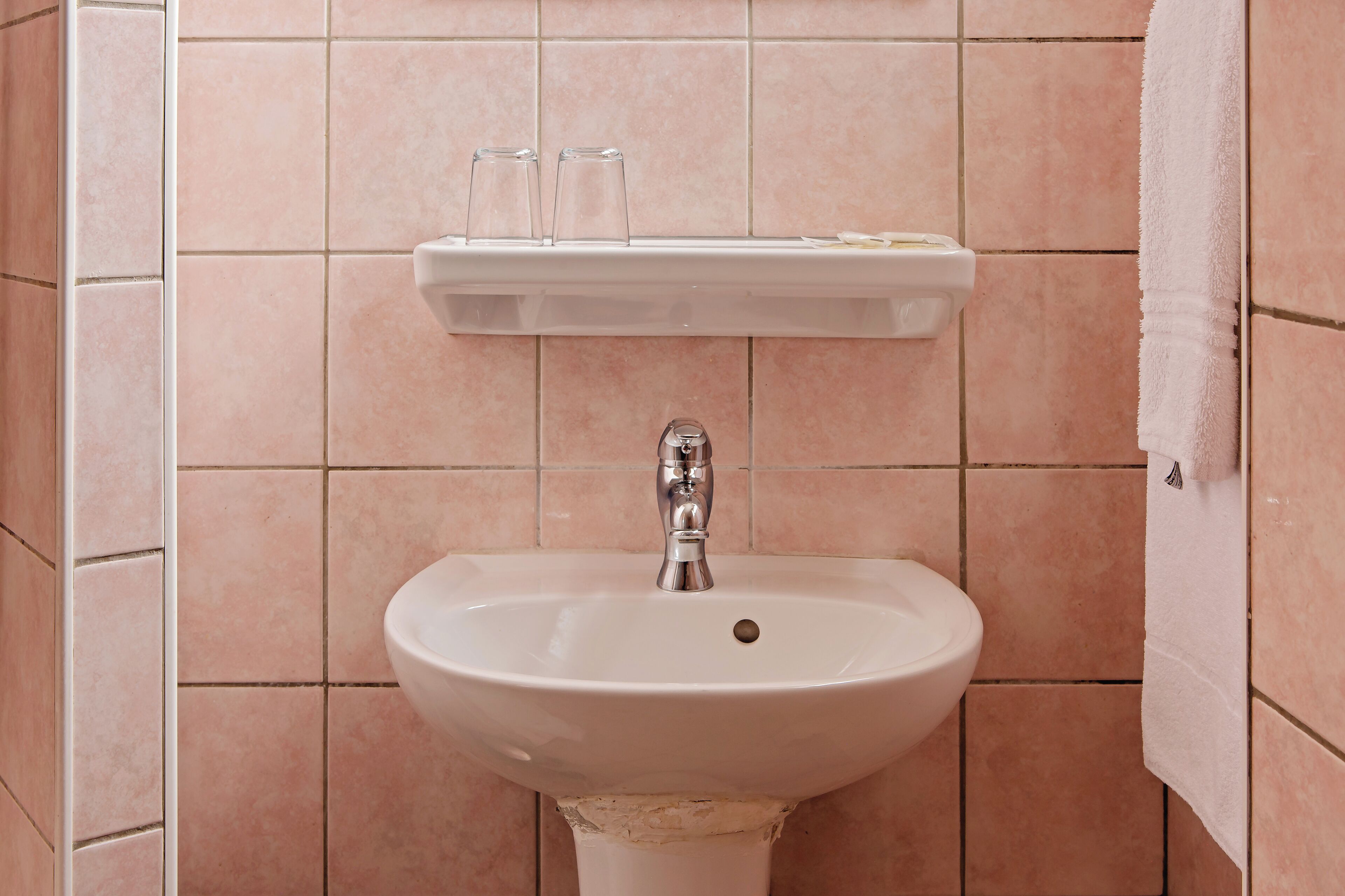 Un baño con lavamanos blanco, un espejo y un estante sobre el lavamanos.