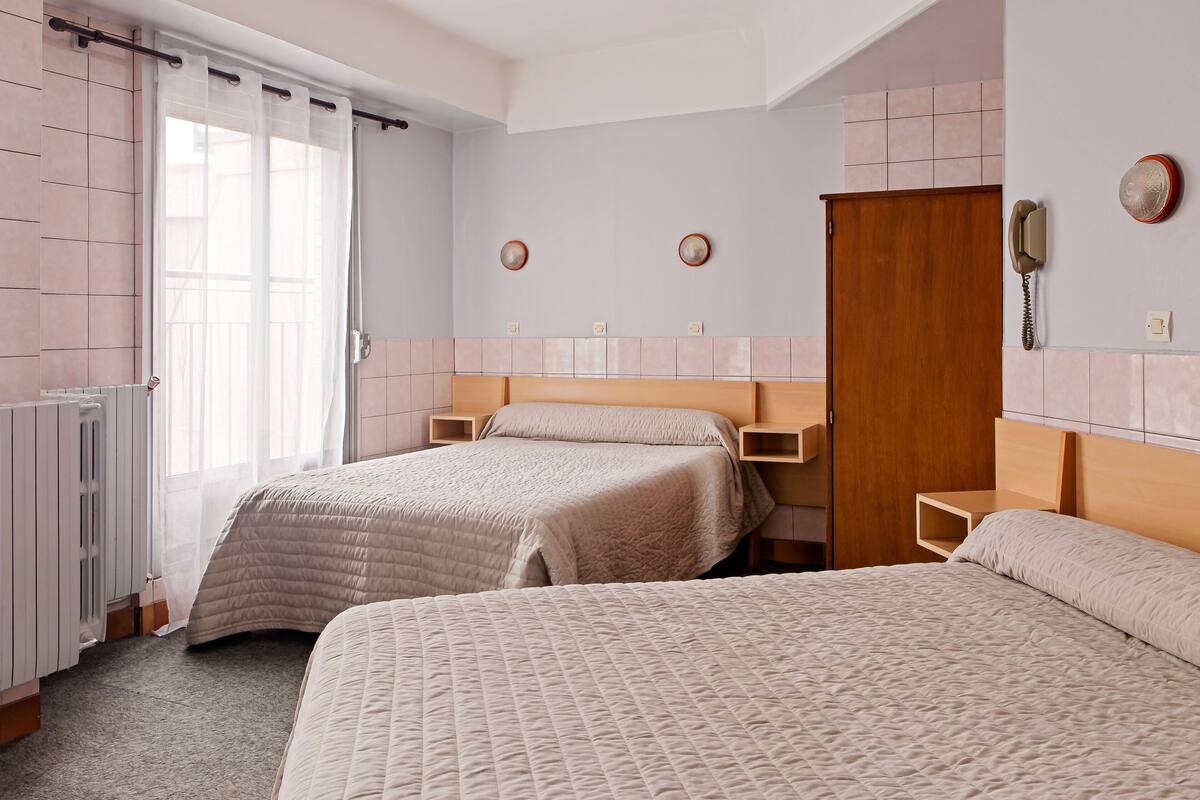 A bedroom with two beds, a wooden door, a radiator, and a telephone on the wall.