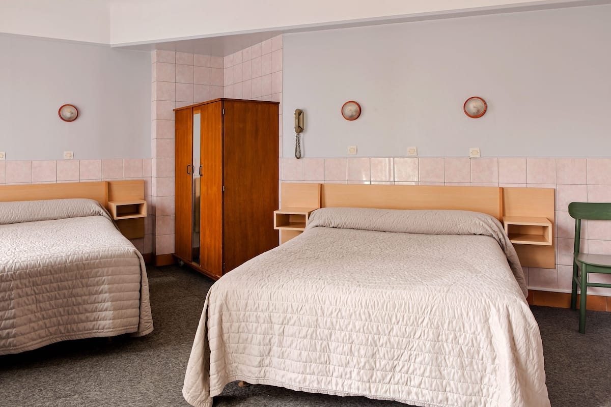 A hotel room with two beds, a wooden wardrobe, a telephone, and a green chair.