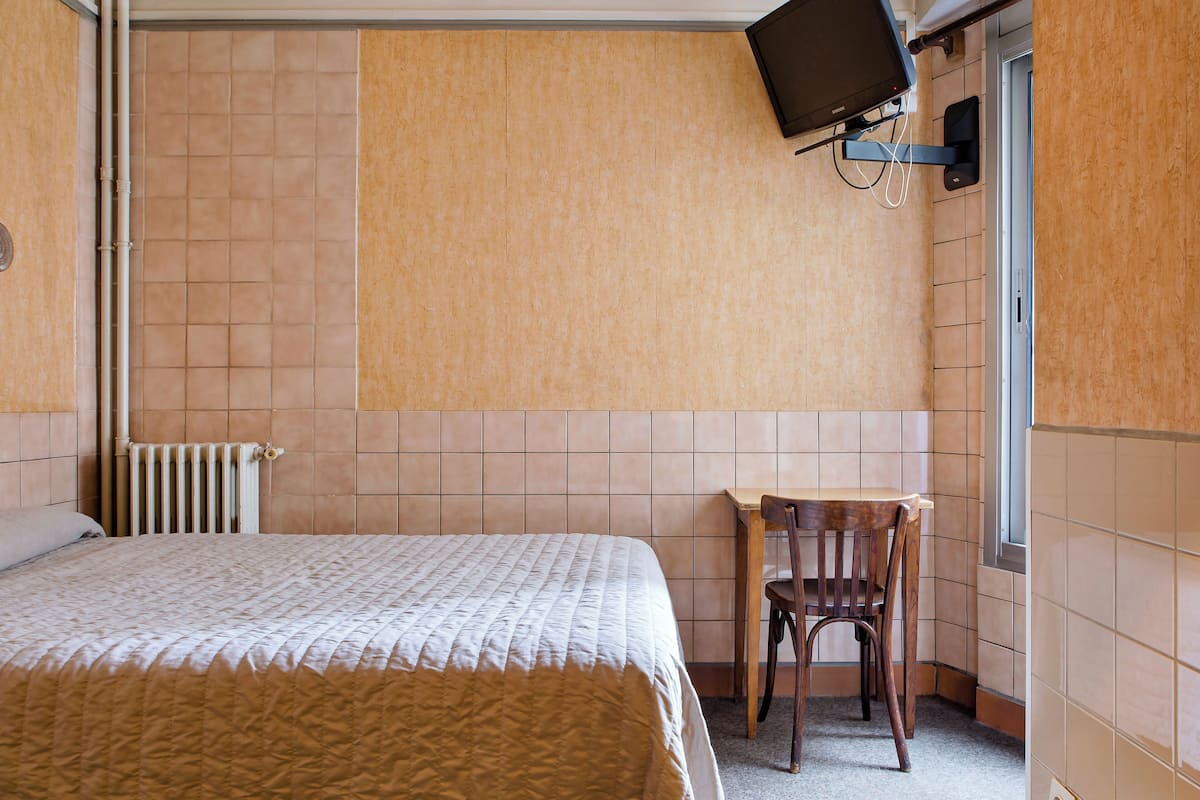 A room with a bed, a chair, a television mounted on the wall, and a radiator.