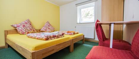 Habitación individual con una cama de madera, ropa de cama amarilla y una silla roja.