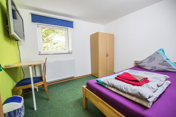 A small, tidy room with a bed, a wooden wardrobe, a desk, and a radiator. - Hotel Burghof (Stolberg)