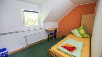 Una habitación pequeña y bien iluminada con una cama individual, un escritorio y una ventana.