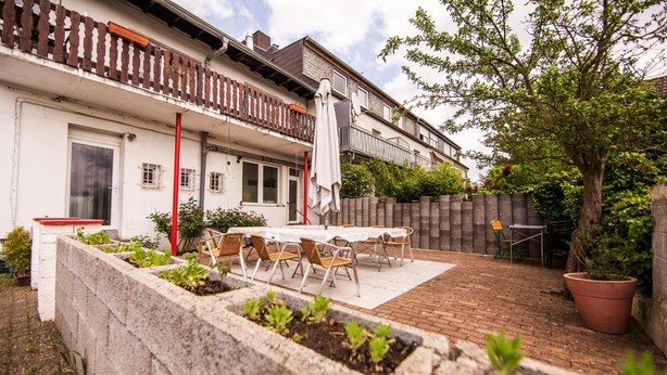 A patio with outdoor seating, a white building with a balcony, and a brick wall. - Hotel Schwan (Eschweiler)