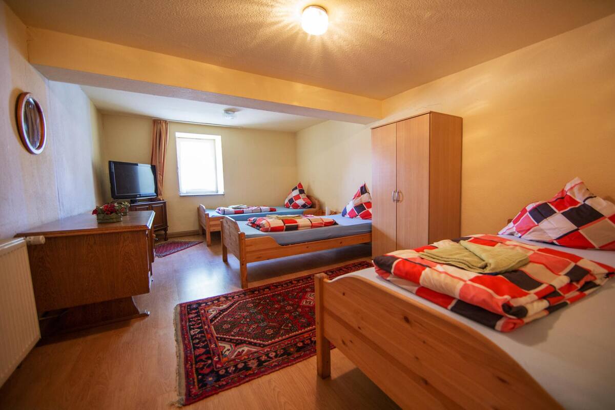Ein gemütliches Zimmer mit zwei Einzelbetten, einem Holzschrank, einem Fernseher und einem gemusterten Teppich.