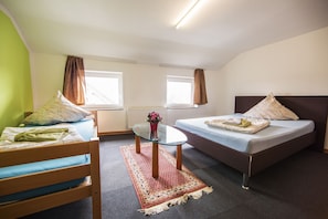 A small, well-lit room with a bed, a chair, a table with a vase, and two windows. - Hotel Schwan (Eschweiler)