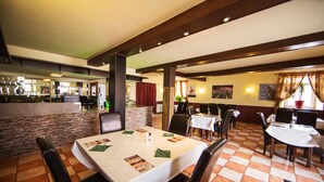 A restaurant with a bar area, stone wall, and tiled floor. Tables are set with menus and cutlery. - Hotel Schwan (Eschweiler)