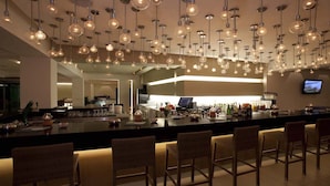 Un espace bar moderne avec des luminaires suspendus, un long comptoir et plusieurs tabourets de bar.