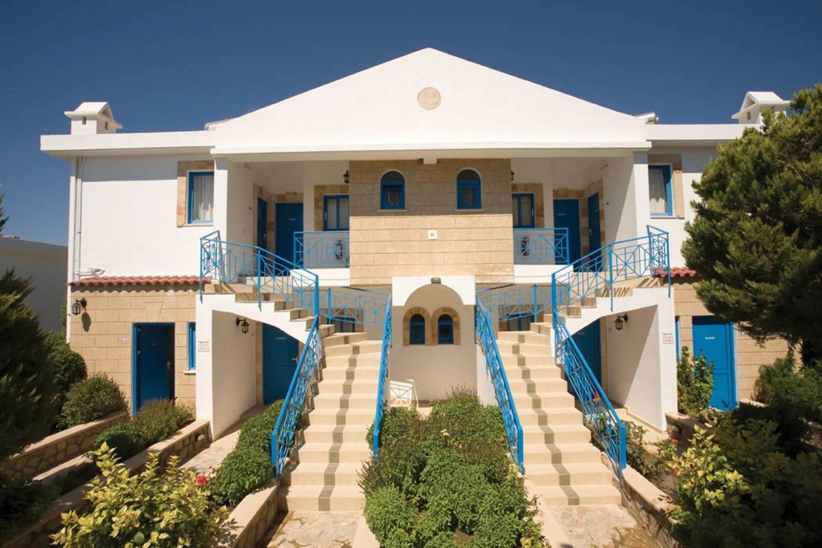 Un edificio de dos pisos con una escalera central, barandillas azules y fachada blanca.