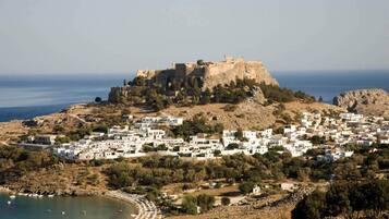 Un pueblo costero con un castillo destacado en una colina, rodeado de edificios blancos y una pequeña playa.