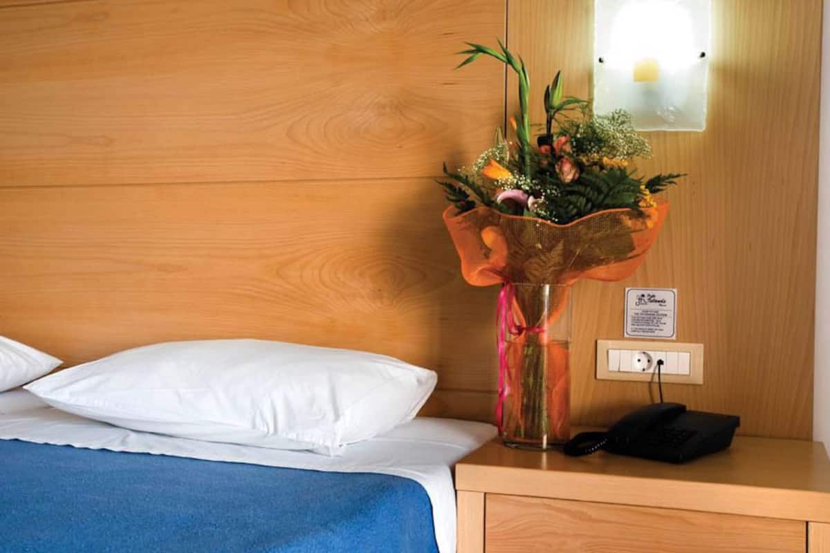 Une chambre d’hôtel avec une tête de lit en bois, un lit avec des oreillers blancs et une couvre-lit bleue, une table de chevet avec un téléphone et un bouquet de fleurs dans un panier.