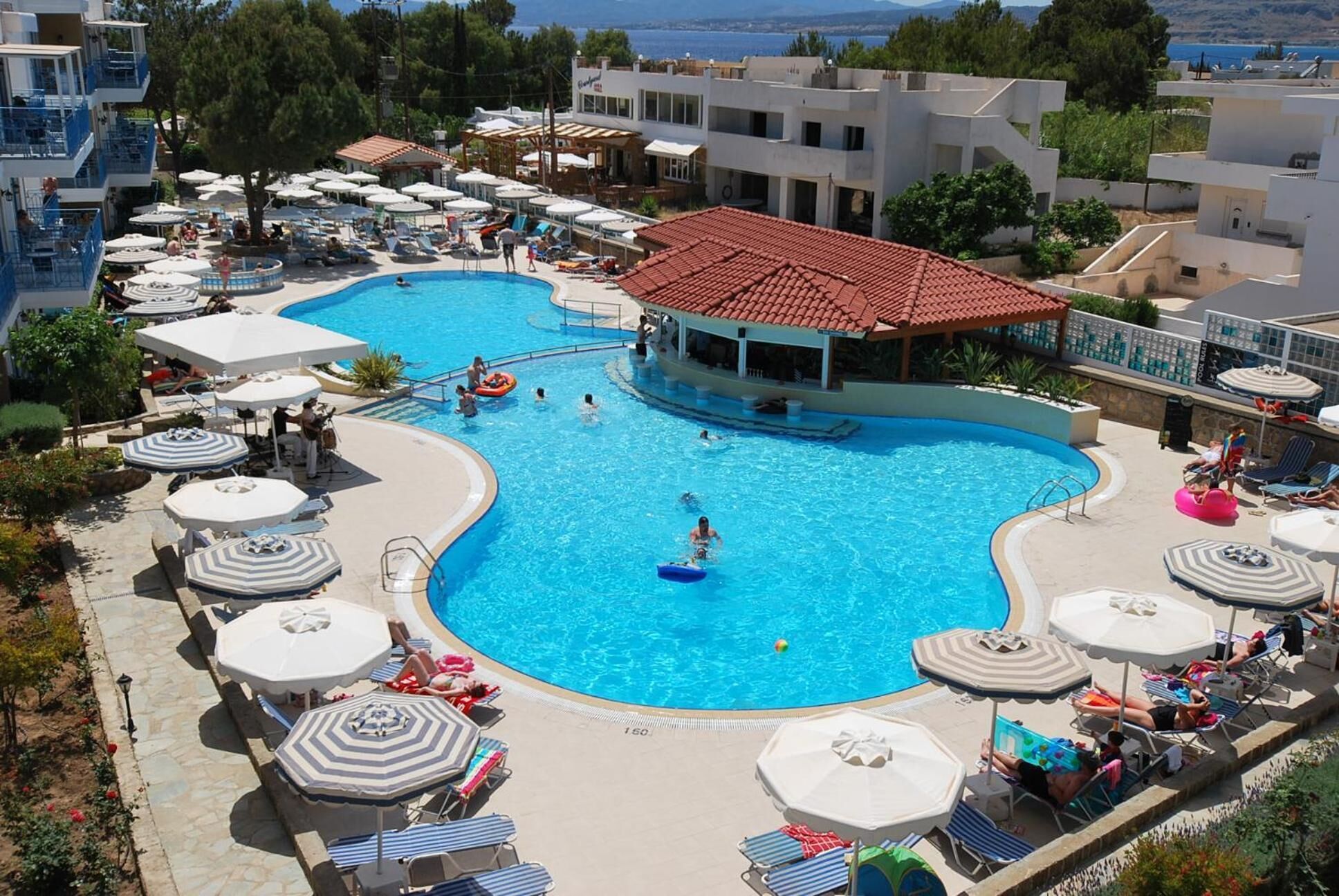 A large swimming pool surrounded by lounge chairs and umbrellas, with a building in the background.