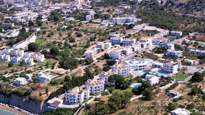 Vue aérienne d’un quartier résidentiel situé sur la côte, avec de nombreux bâtiments blancs, dont certains sont dotés de balcons, et une mer d’un bleu limpide.