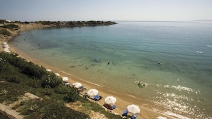 Une plage avec une eau cristalline, des gens qui se baignent et des parasols de plage.