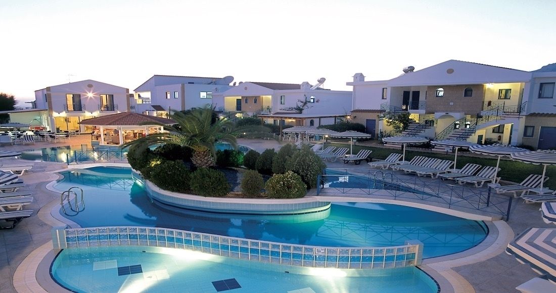 A hotel with a large swimming pool, sun loungers, and a landscaped garden area.