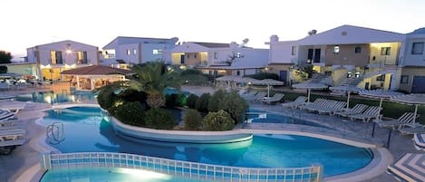 A hotel with a large swimming pool, sun loungers, and a landscaped garden area.