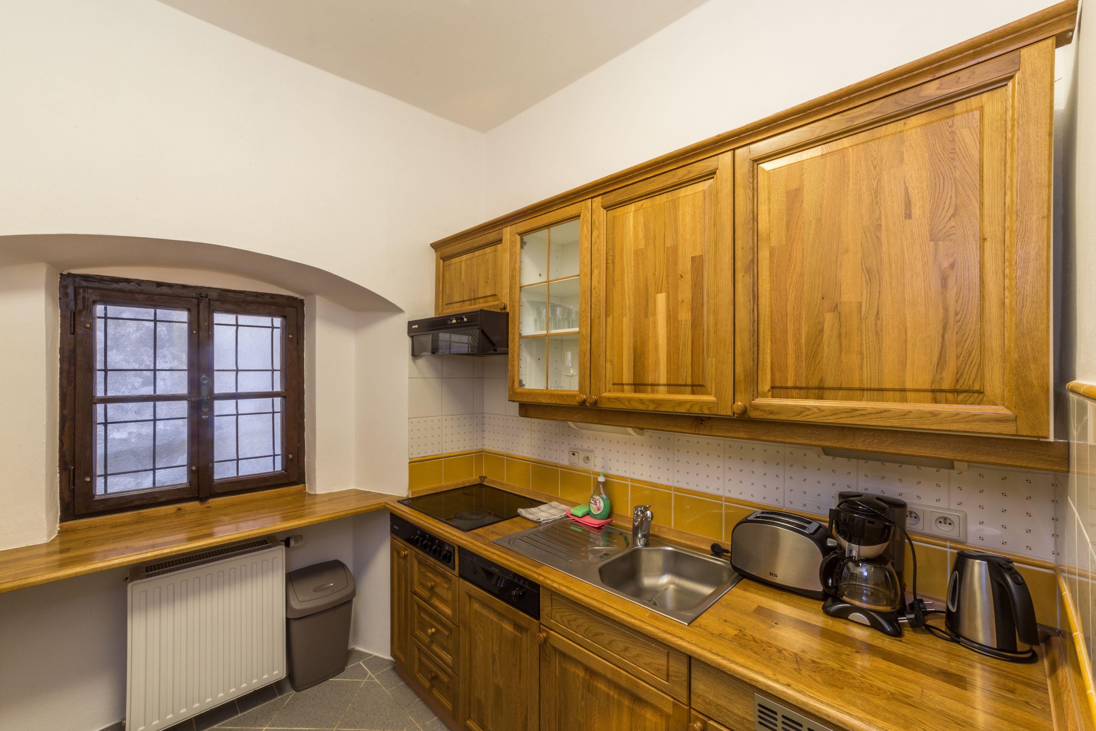 A kitchen with wooden cabinets, a stainless steel sink, a coffee maker, and a window with a view.